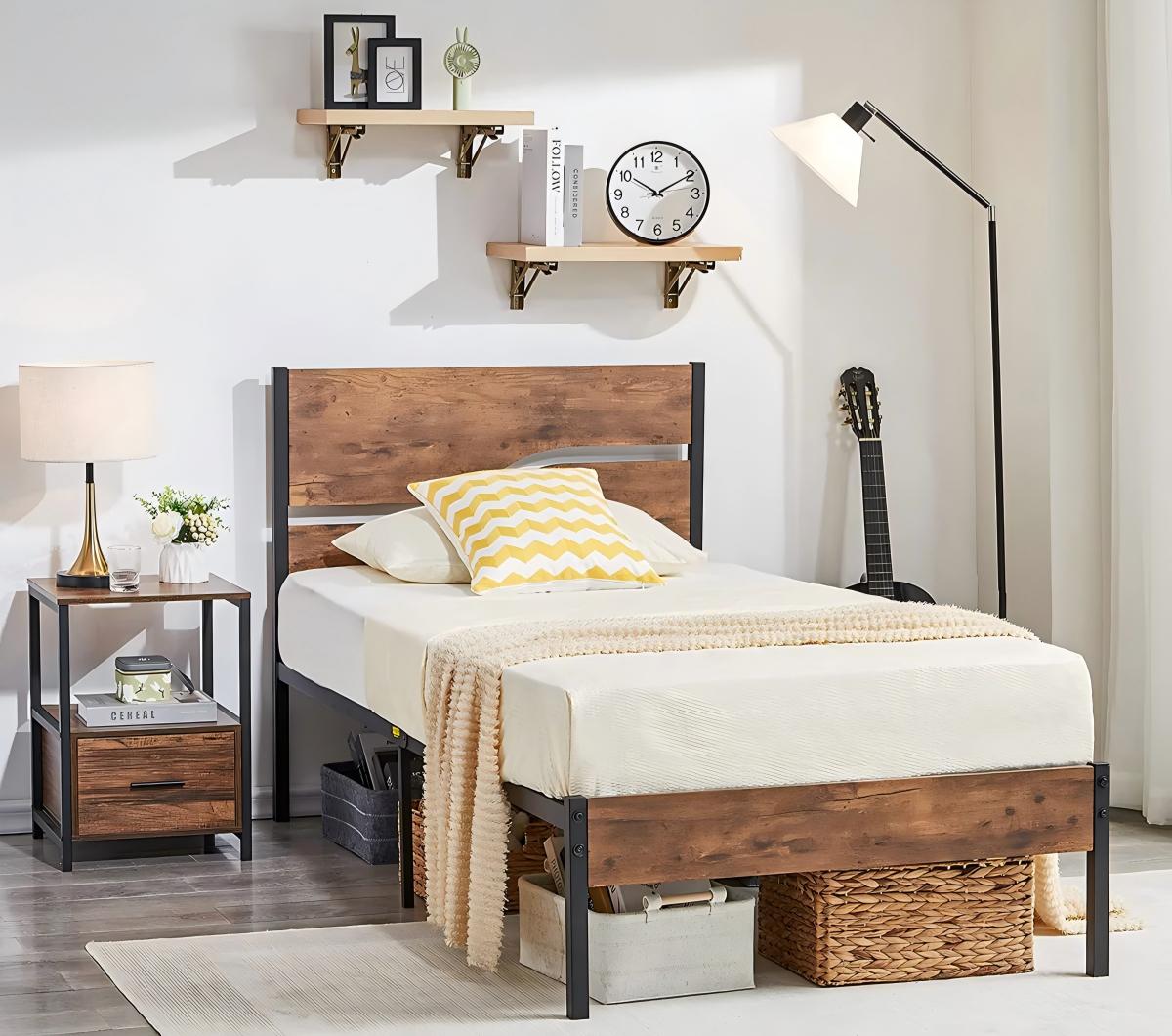 Rustic industrial twin bed with wood headboard and black metal frame, styled with neutral bedding, bedside table, floor lamp, wall shelves, and under-bed storage baskets in a minimalist bedroom.