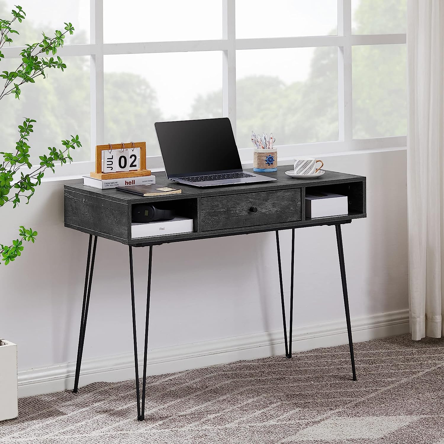 A VECELO modern dark wood writing desk with slim black metal legs, featuring open storage compartments and a center drawer, styled with a laptop, books, and coffee cup by a bright window.